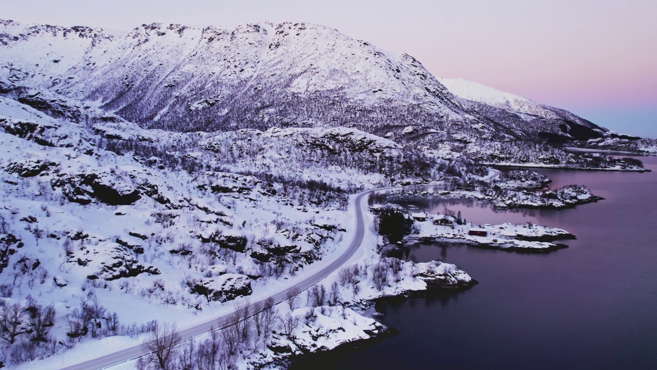 黑色SUV行驶在白雪皑皑的沿海道路上，背景是夕阳色的天空。视频素材