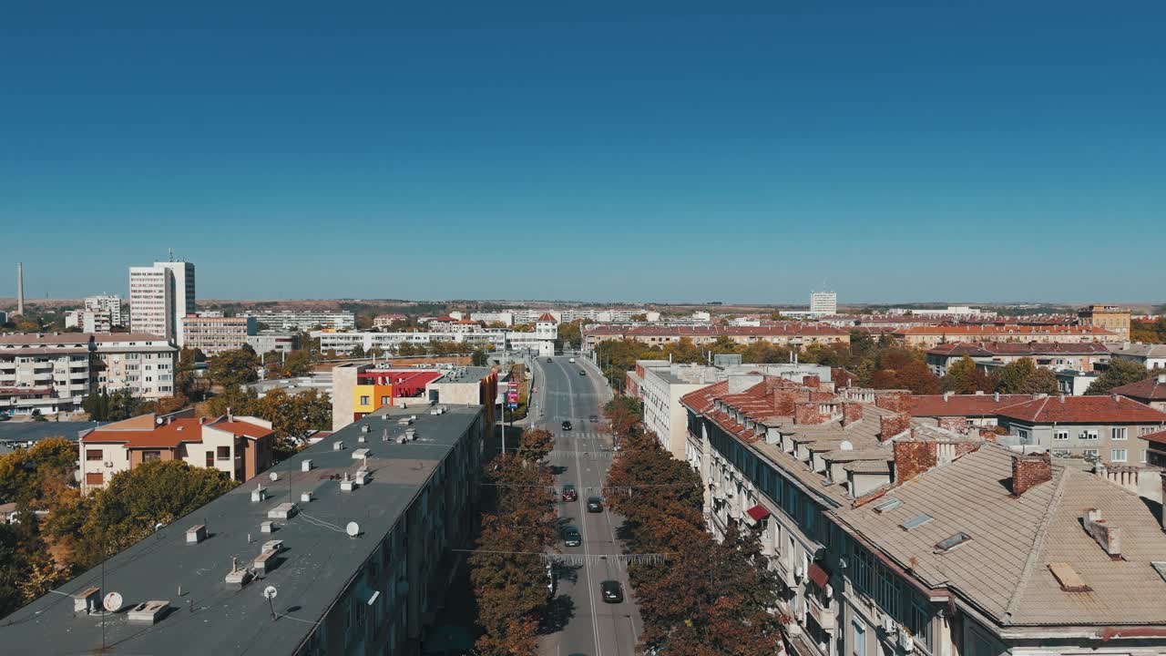 无人机拍摄的鸟儿飞过季米特洛夫格勒的城市景观，路上有秋天的树木和汽车视频素材