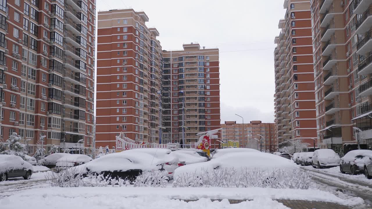 道路和汽车被积雪覆盖在多层建筑的院子里。视频素材