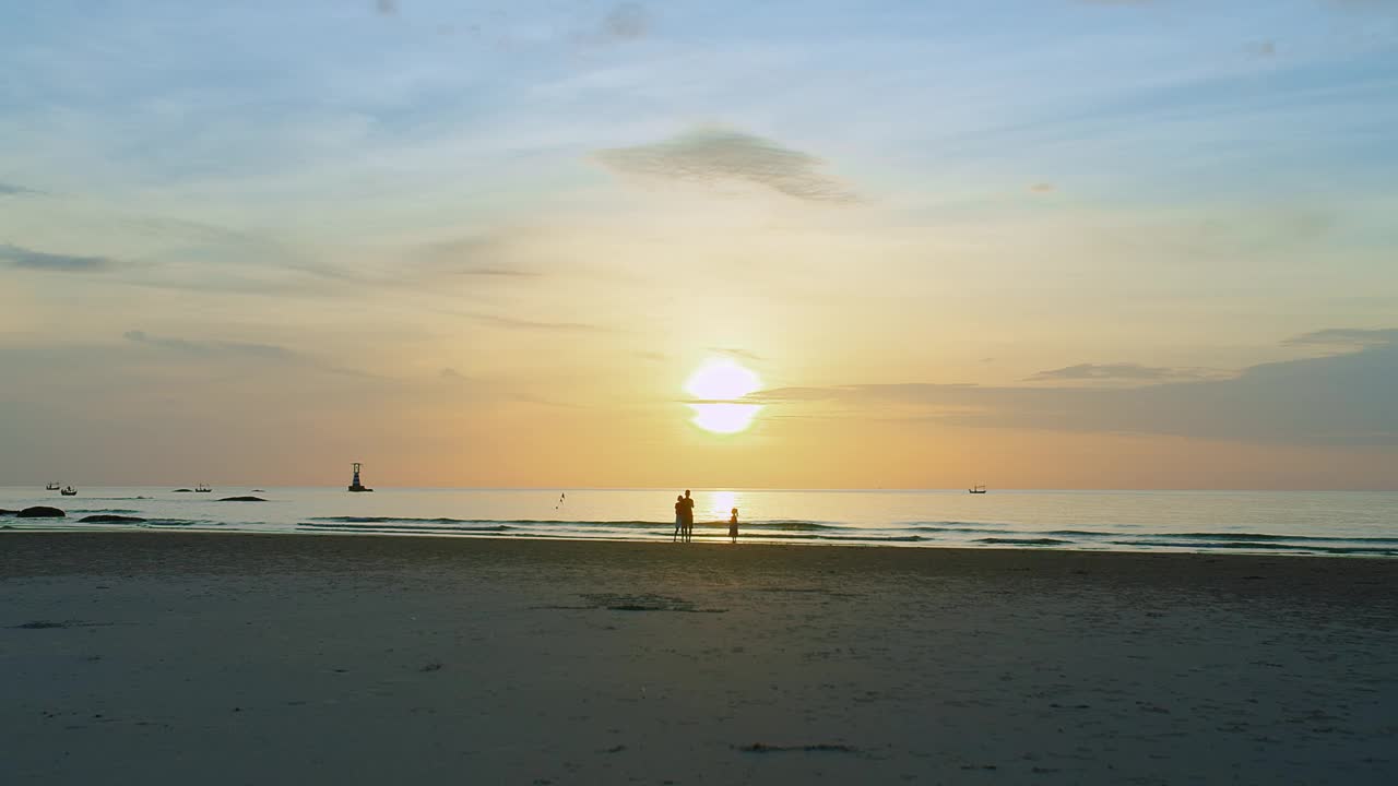 宁静的海滩风景，宁静的日落海景，家人享受这一刻，他们的剪影映衬着金色的天空，传达出一种自由与和平的感觉视频素材