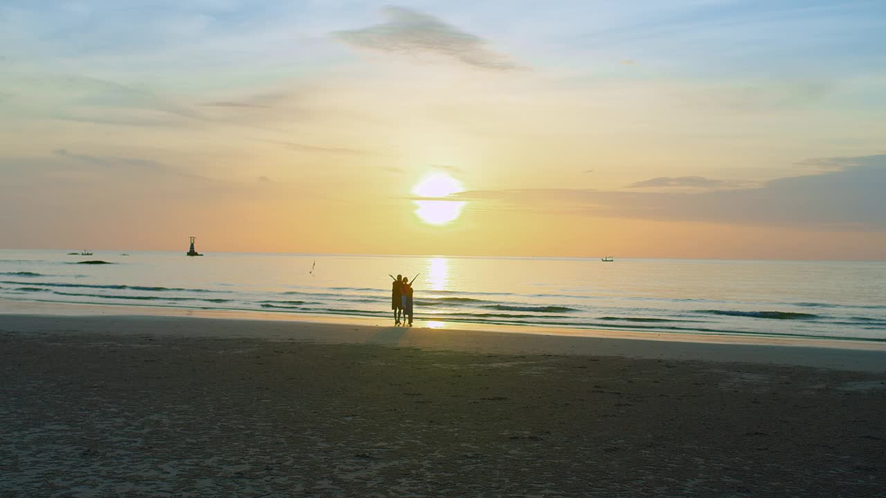 宁静的海滩风景，宁静的日落海景，家人享受这一刻，他们的剪影映衬着金色的天空，传达出一种自由与和平的感觉视频素材