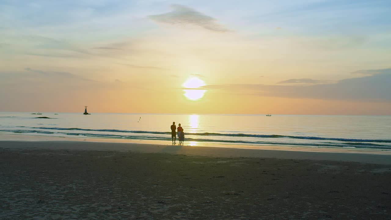 宁静的海滩风景，宁静的日落海景，家人享受这一刻，他们的剪影映衬着金色的天空，传达出一种自由与和平的感觉视频素材