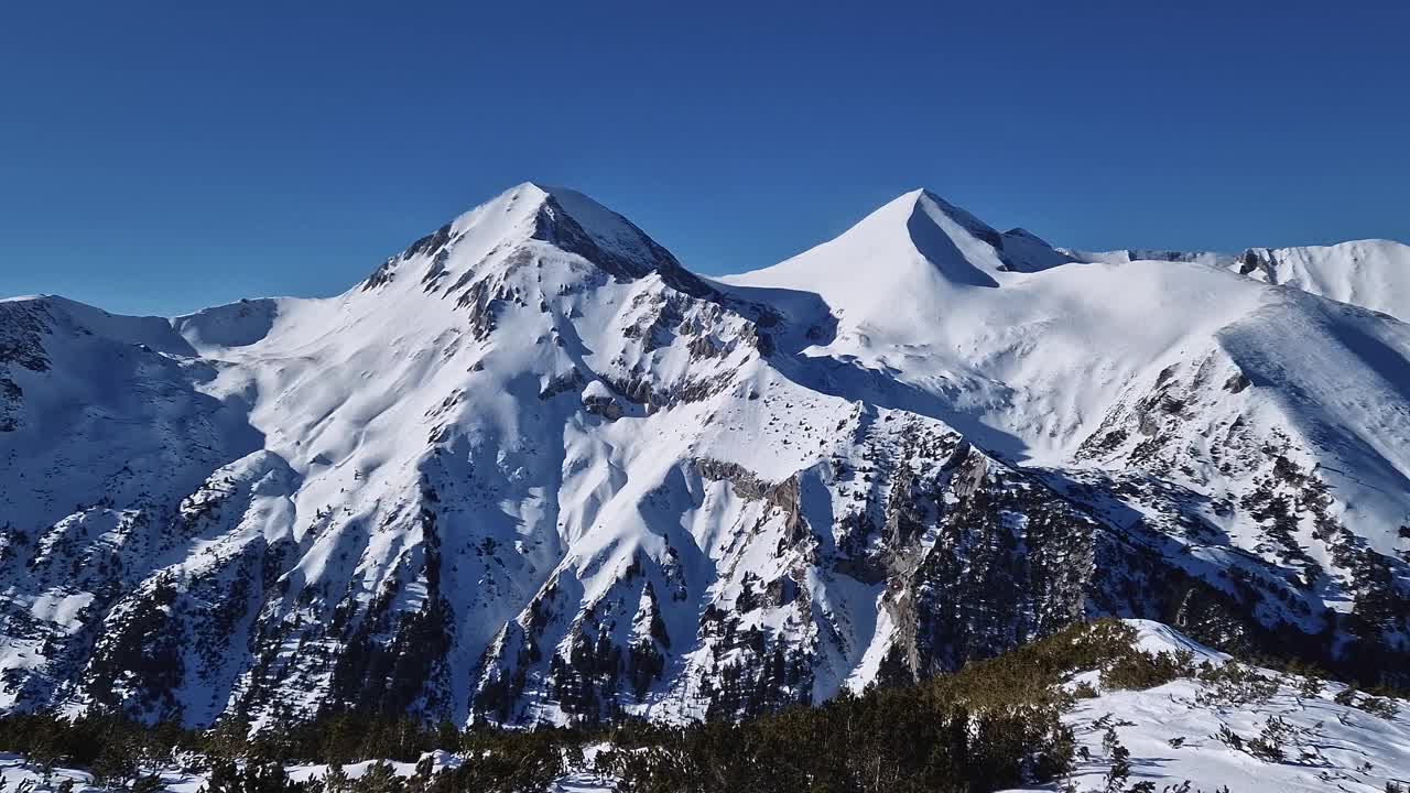 从空中俯瞰皮林山脉，岩石山峰被雪覆盖。保加利亚班斯科滑雪胜地的冬季景色视频素材