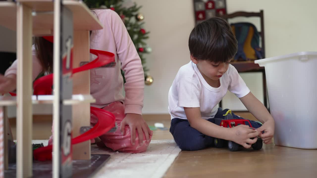 专心的男孩在客厅地板上和妹妹兄弟姐妹一起玩他的卡车玩具，坦率的孩子们从事游戏，童年的休闲活动视频素材