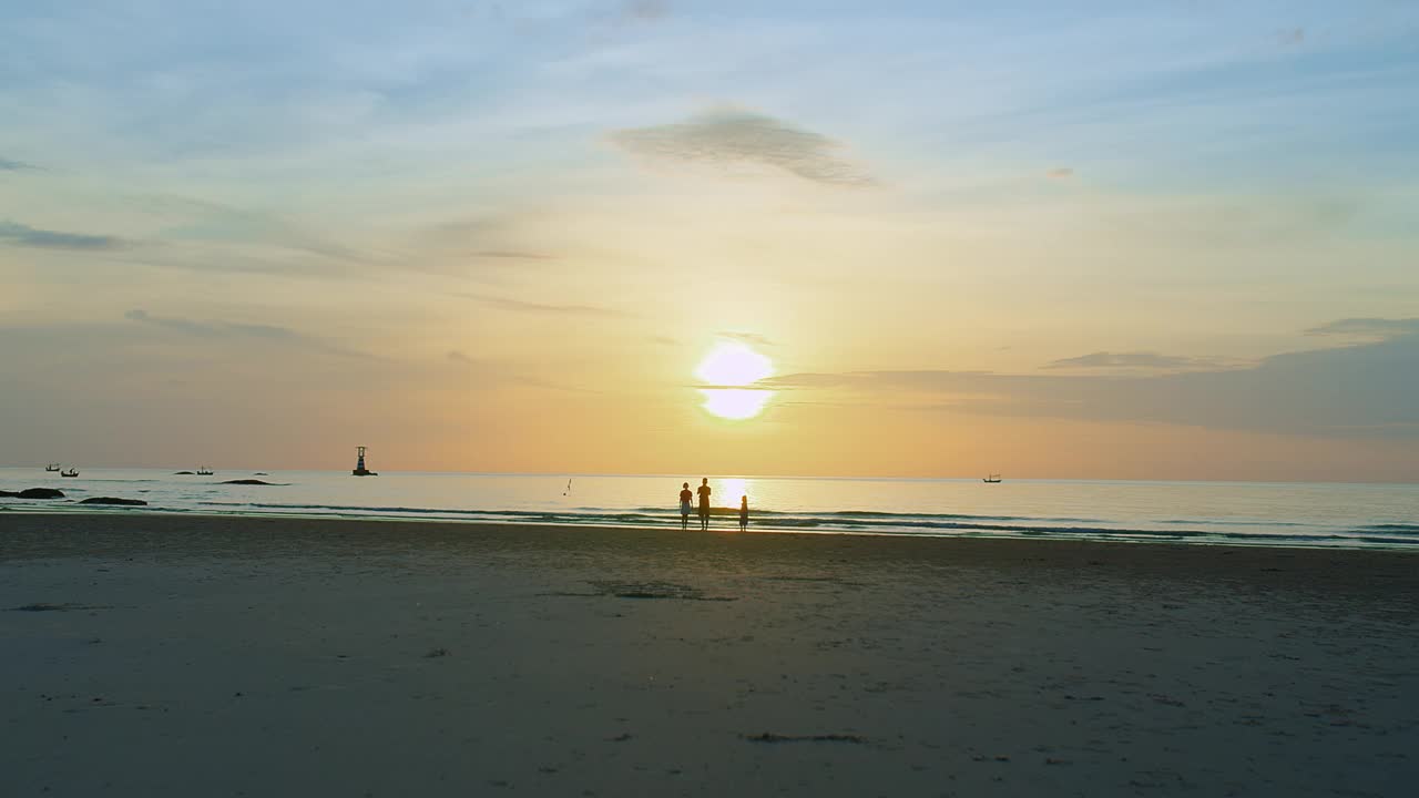 宁静的海滩风景，宁静的日落海景，家人享受这一刻，他们的剪影映衬着金色的天空，传达出一种自由与和平的感觉视频素材