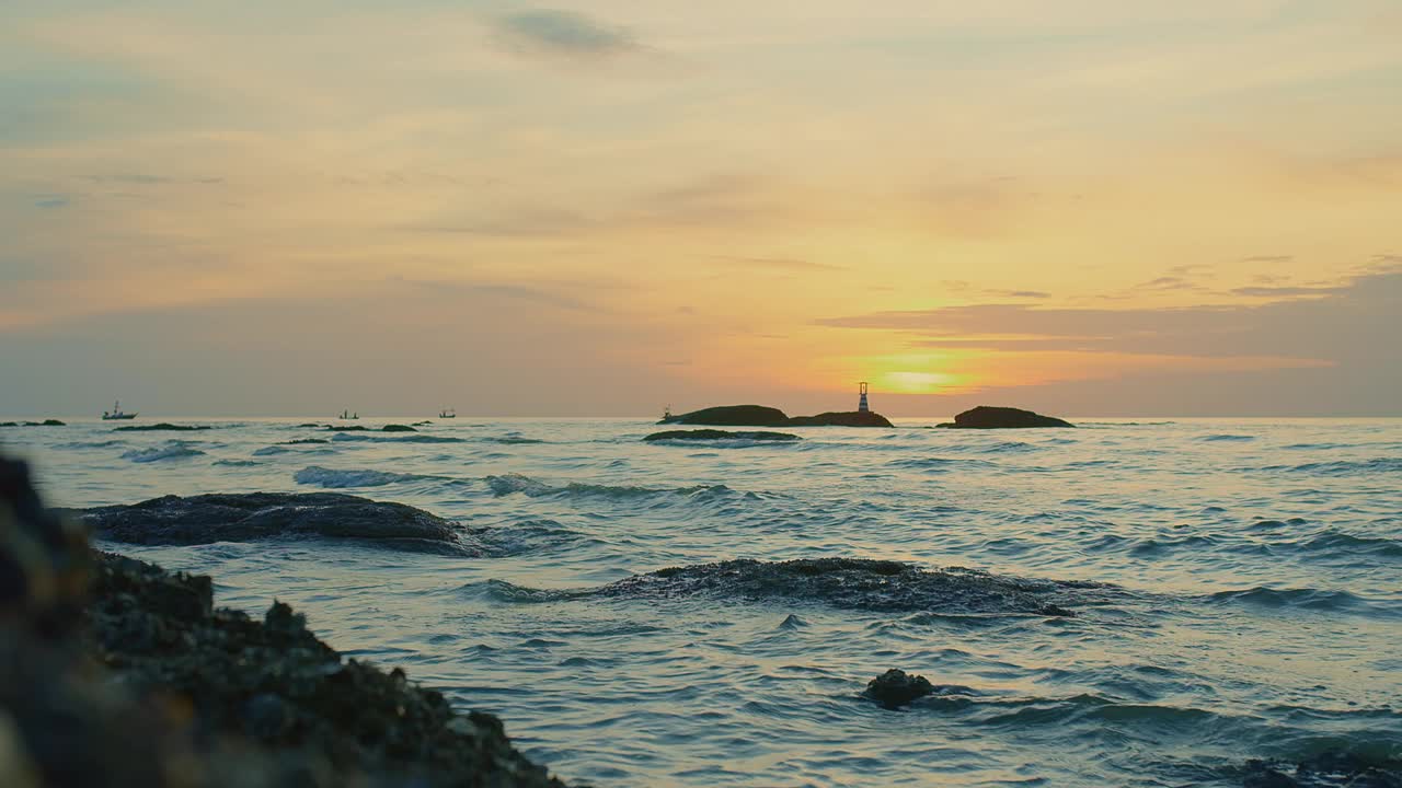 日落时宁静的海景，海浪轻轻地拍打着岩石，远处有灯塔的剪影视频素材