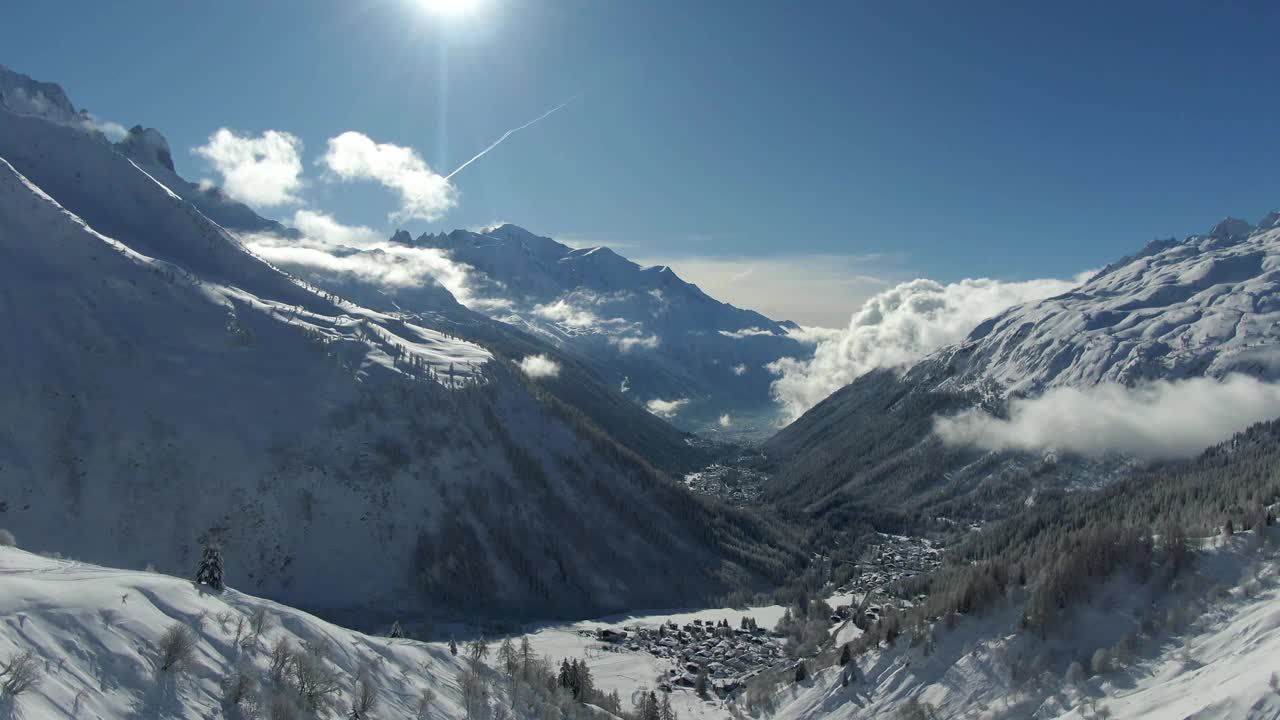 无人机镜头在雪谷与遥远的山脉，阳光明媚的天空，和绿树成荫的斜坡视频素材