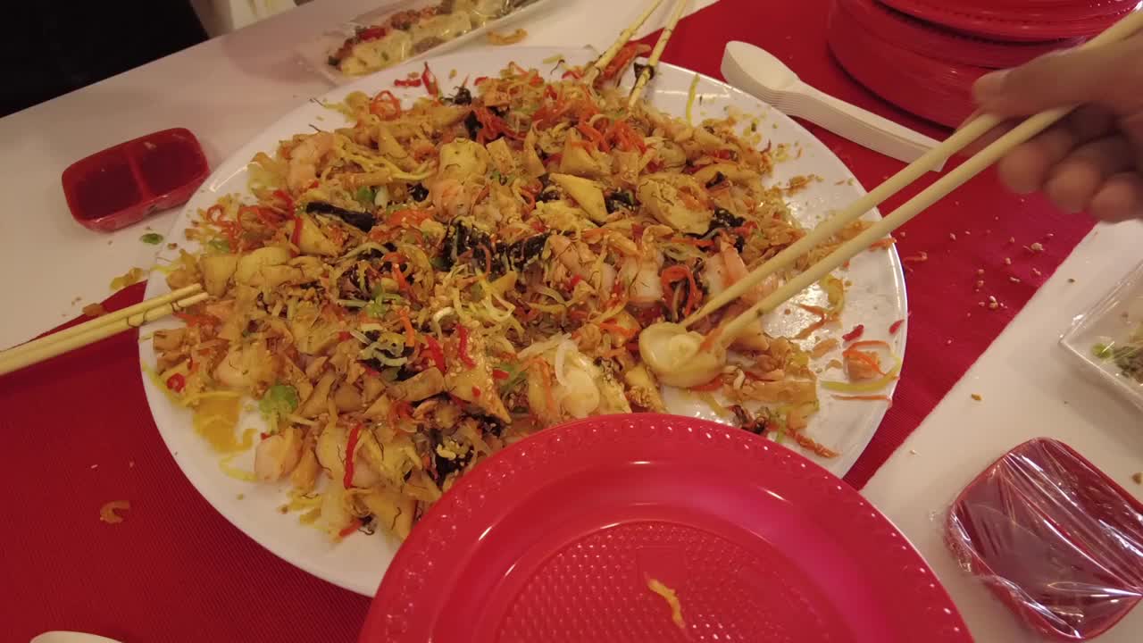 春节庆祝活动期间，人们用筷子从一盘鱼生中取出食材，繁荣地将生鱼沙拉放入红色塑料盘子中视频素材