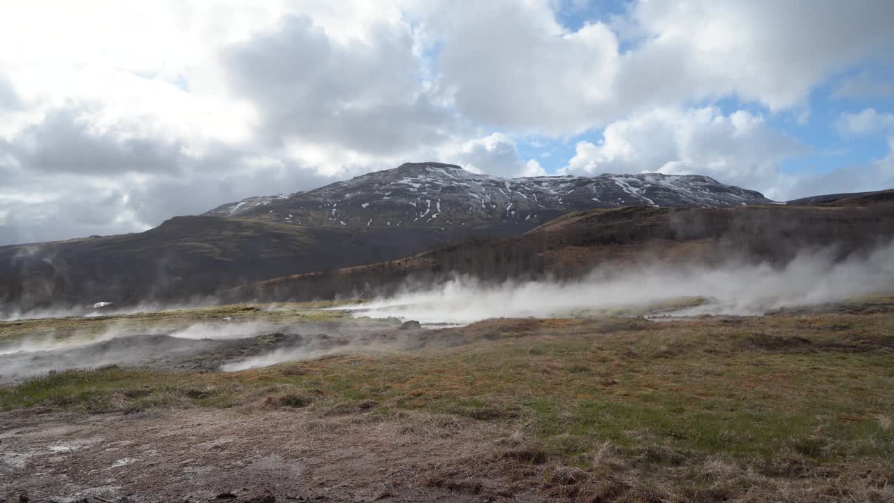 冰岛的地热活动，蒸汽从地面升起，背景是山脉和多云的天空视频素材