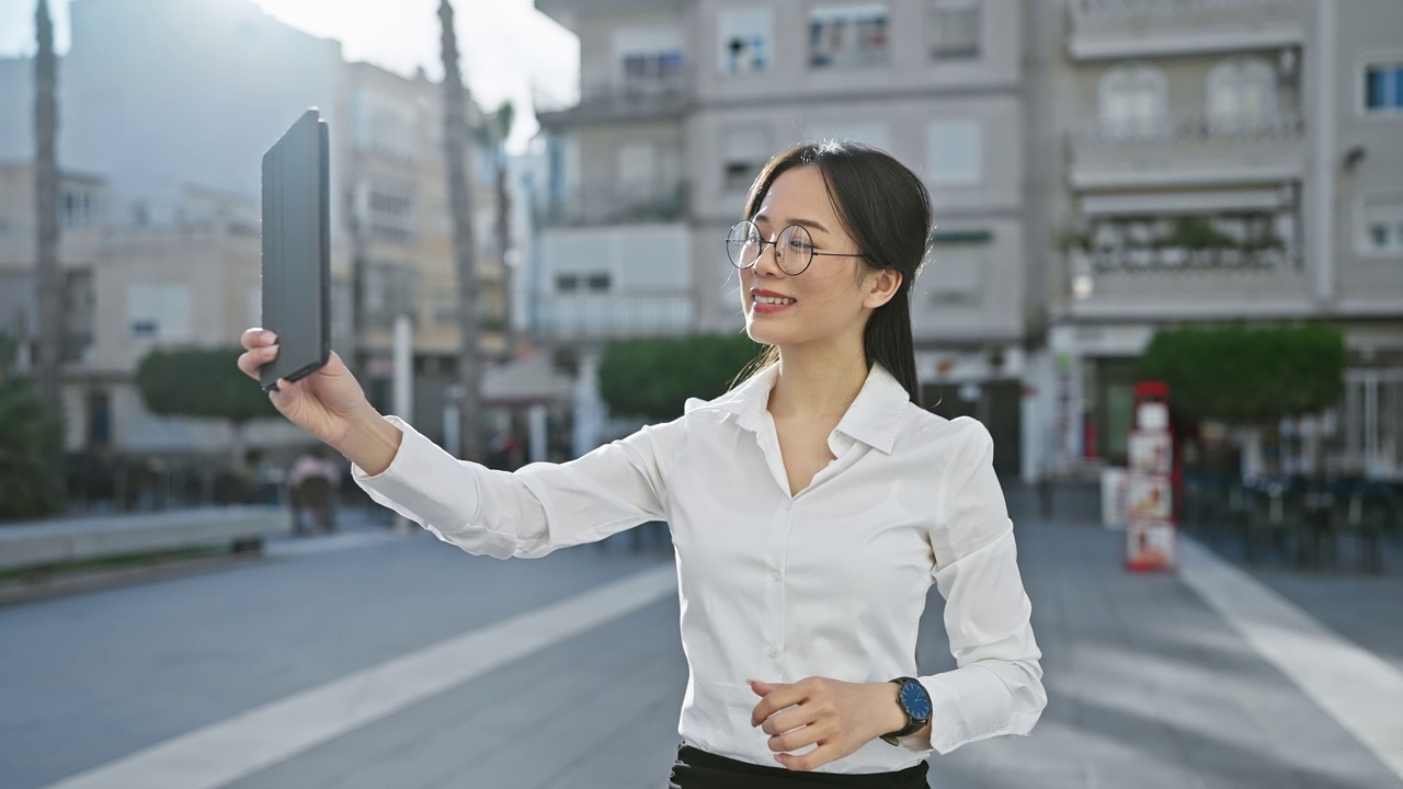 戴眼镜的亚洲妇女在阳光明媚的城市街道上使用平板电脑视频素材