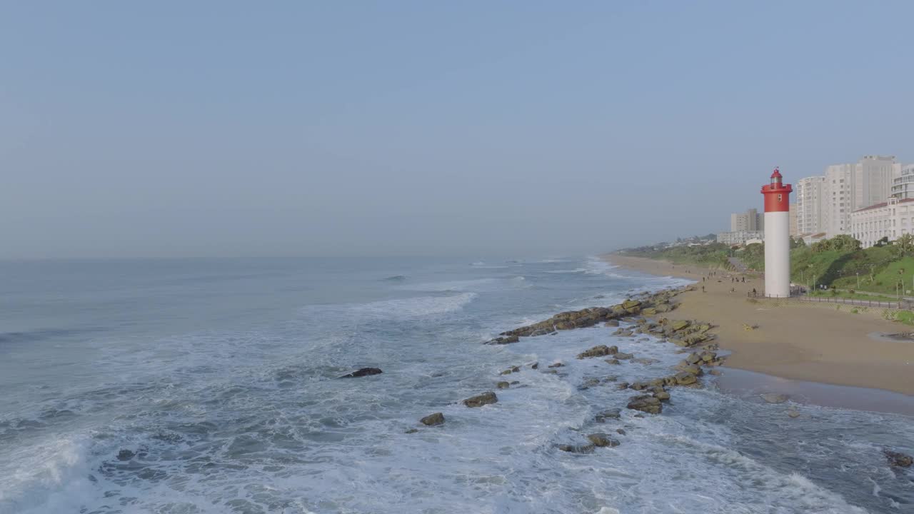 在一个阳光明媚的日子里，海浪冲击着海岸，乌姆兰加灯塔，城市背景，鸟瞰视频素材