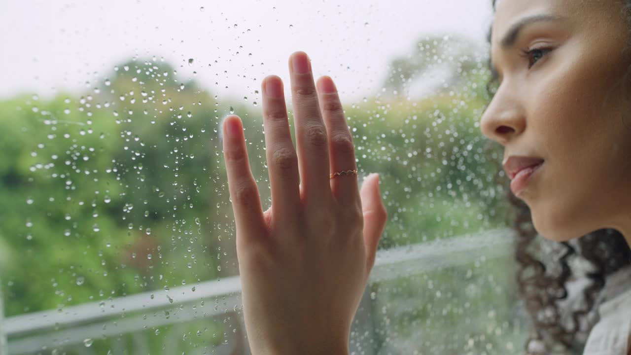 悲伤，女人和思考与手在窗户为雨天，沮丧或错误在室内的家。心理健康或焦虑的年轻女性在家中向外看或触摸玻璃的特写视频素材