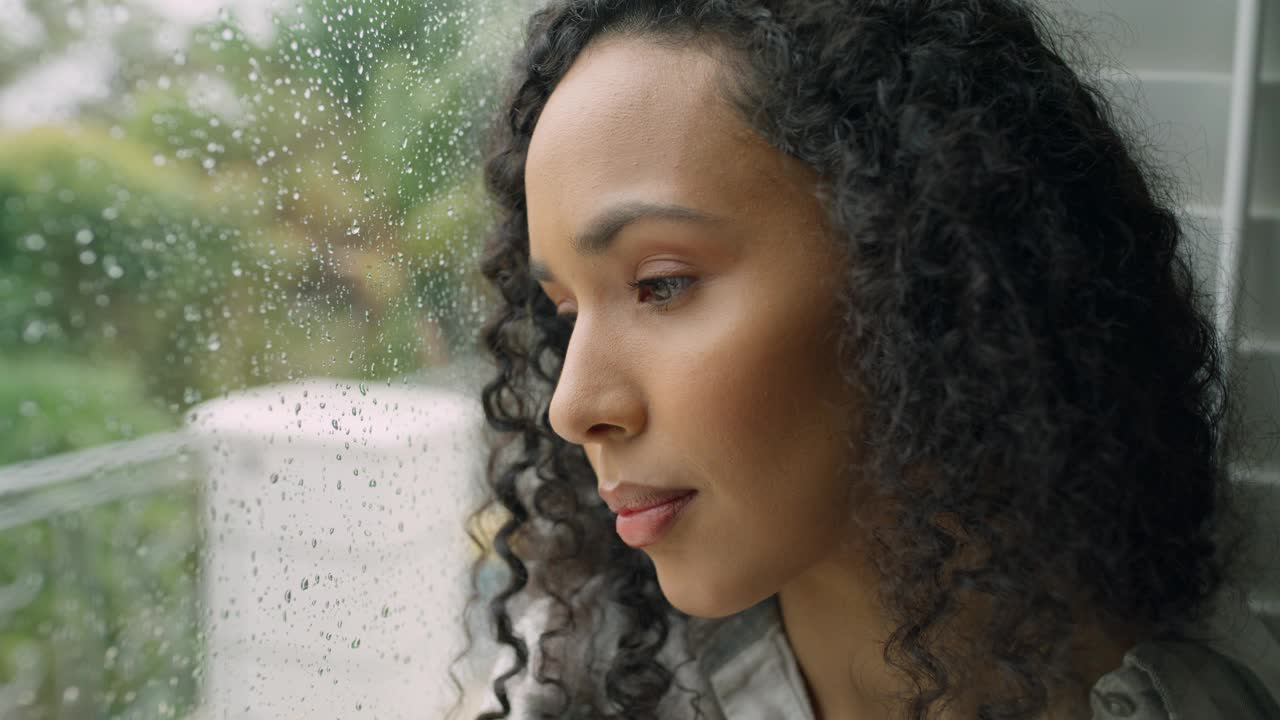 女人，面对和思考忧郁，压力或焦虑下雨或天气在室内的家。年轻女性在疲劳、下雨或心理健康的情况下在家中向外看的特写视频下载