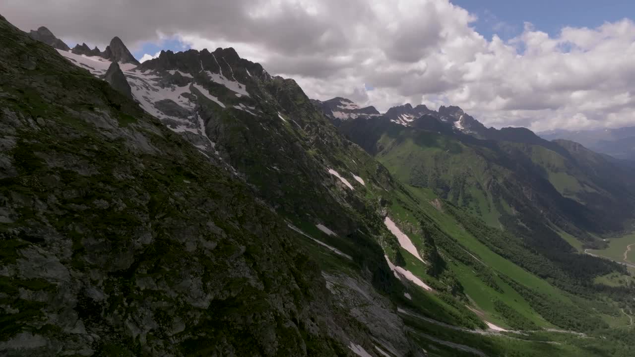 美丽的绿色平原与即使在夏天也不融化的雪峰形成鲜明对比。山的夏季景观与蓬松的云和阳光落在山谷视频素材