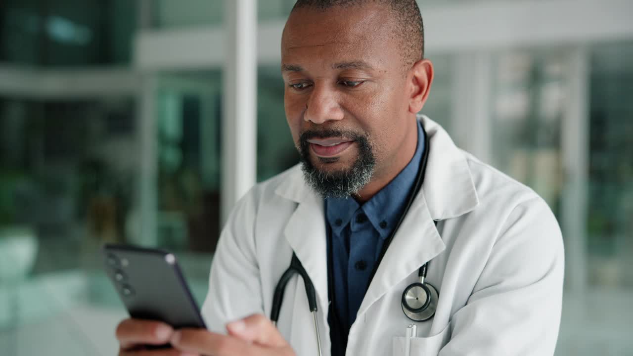 Phone, smile and black man doctor in office with social media, chat or web, scroll or research. Healthcare, smartphone and mature surgeon with app for online consult, faq or telehealth communication视频素材