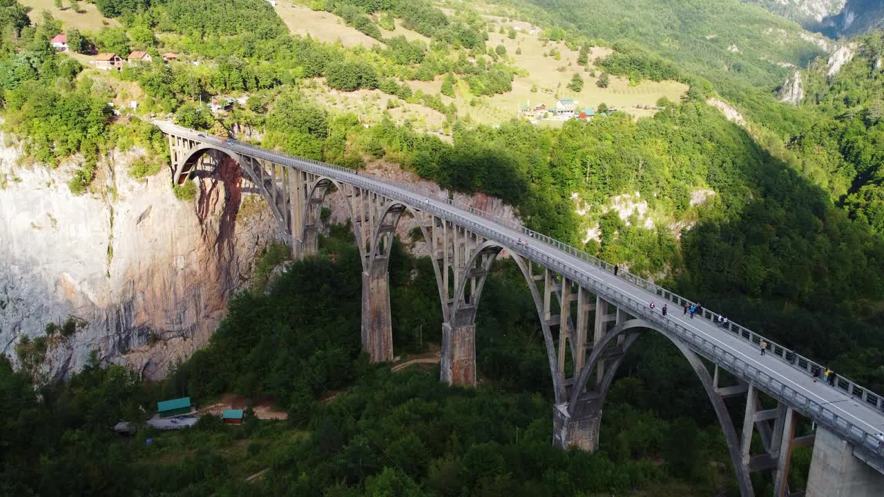在黑山塔拉河峡谷，夏季的绿色景观中，无人机拍摄的拱形Djurdjevica桥上有移动的汽车。杜米托国家公园Zabljak镇附近的热门旅游目的地。视频素材