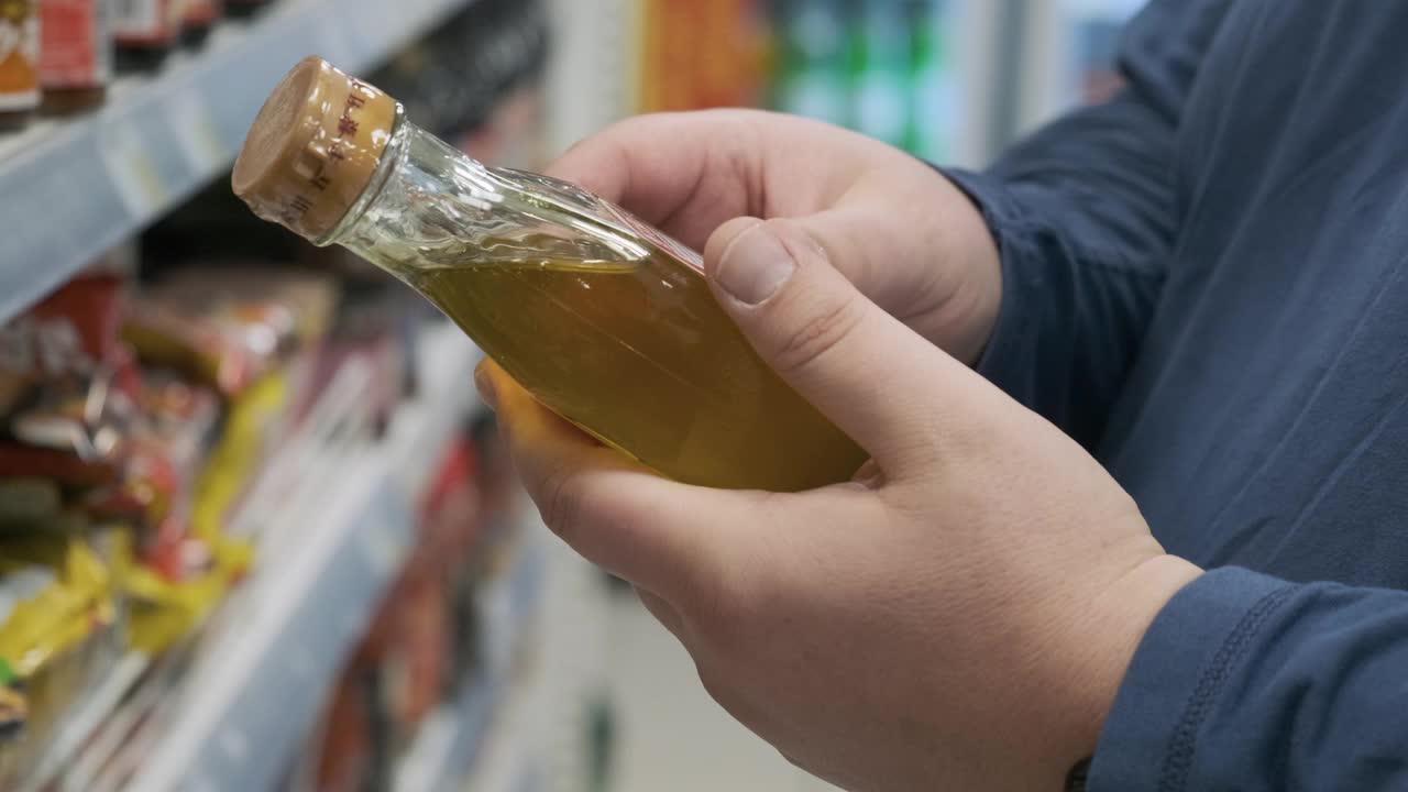 一名男子在超市的货架上挑选装在玻璃瓶里的天然有机植物油视频素材