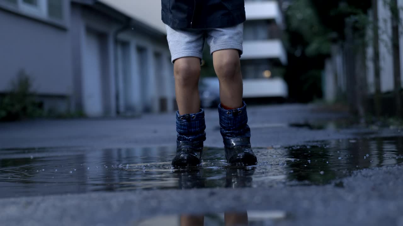 快乐的跳跃-孩子在空中跳到水坑，雨后的慢动作水花以800帧/秒的速度拍摄视频素材