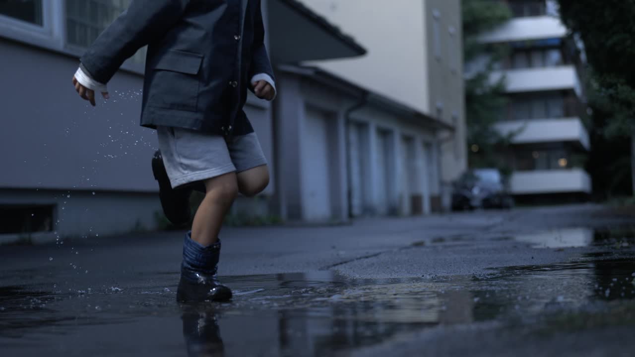 顽皮的孩子穿着雨衣踢水坑。孩子们在雨后玩耍，用慢动作的高速相机捕捉童年的怀旧概念视频素材