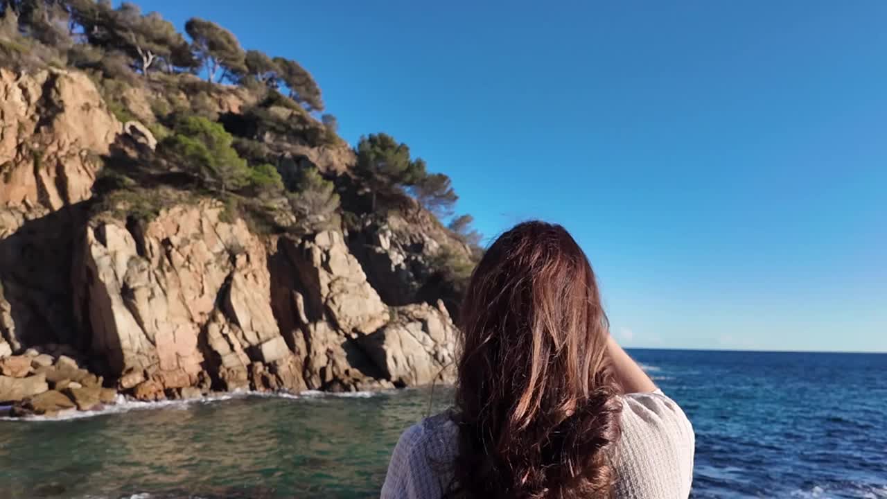 在一个阳光明媚的日子里，一个棕色长发的放松女人走向海边视频素材