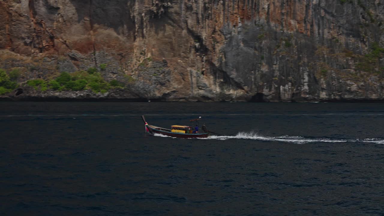 一艘木船在海上，背景是泰国皮皮群岛的岩石海岸。视频素材