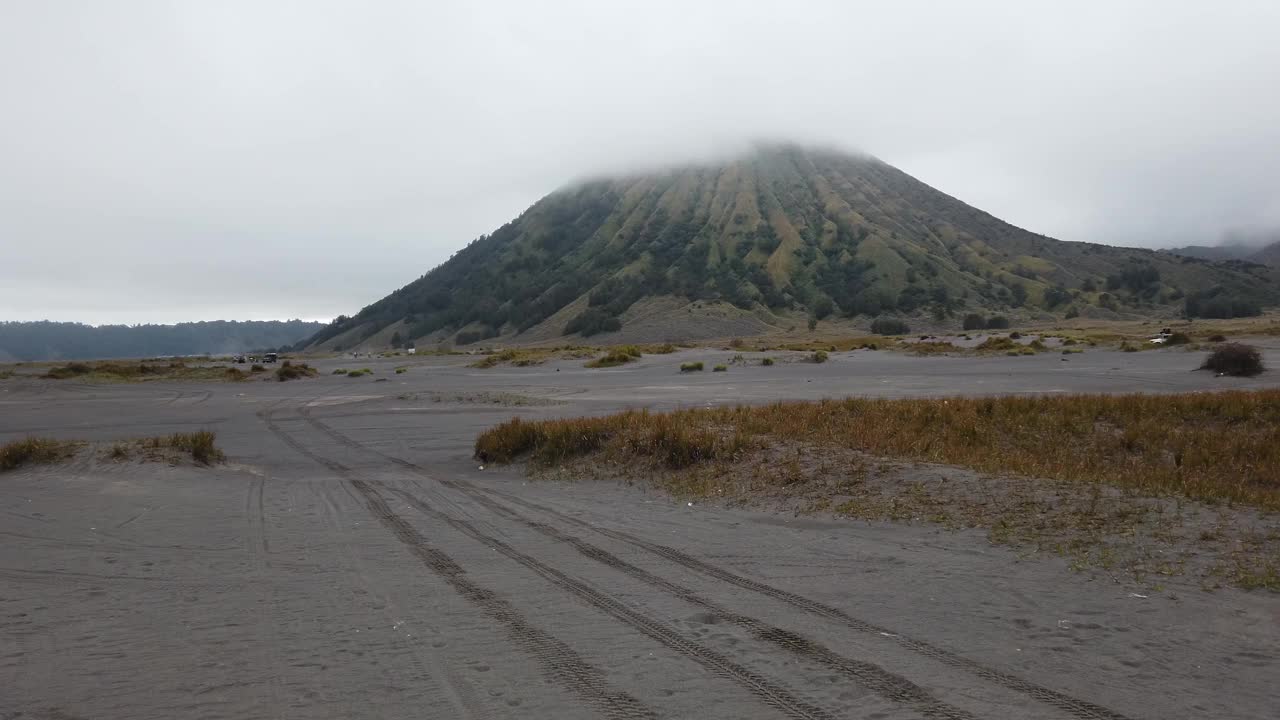 旅游车辆行驶在前往布罗莫山的沙海中。背景中可以看到巴托克火山火山口视频下载