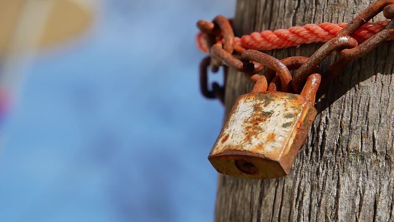 这把旧钥匙又锈又脏。用一条旧铁链和红色尼龙绳锁在一棵大树上。视频素材