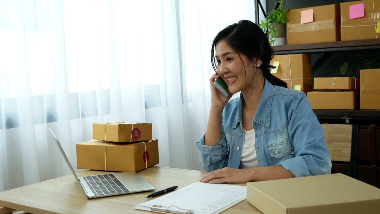 网上卖家近距离接触年轻的亚洲女子，她正在输入笔记本电脑键盘，检查网上订单，检查货物库存，发货包裹，发货邮政。亚洲女性在家办公室做小生意视频素材