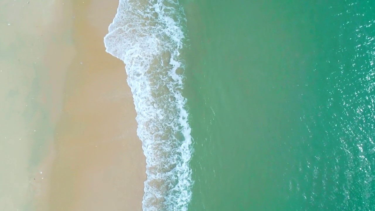 鸟瞰沙滩和蓝绿色海洋。在阳光明媚的日子里海浪到达海岸的俯视图。视频素材