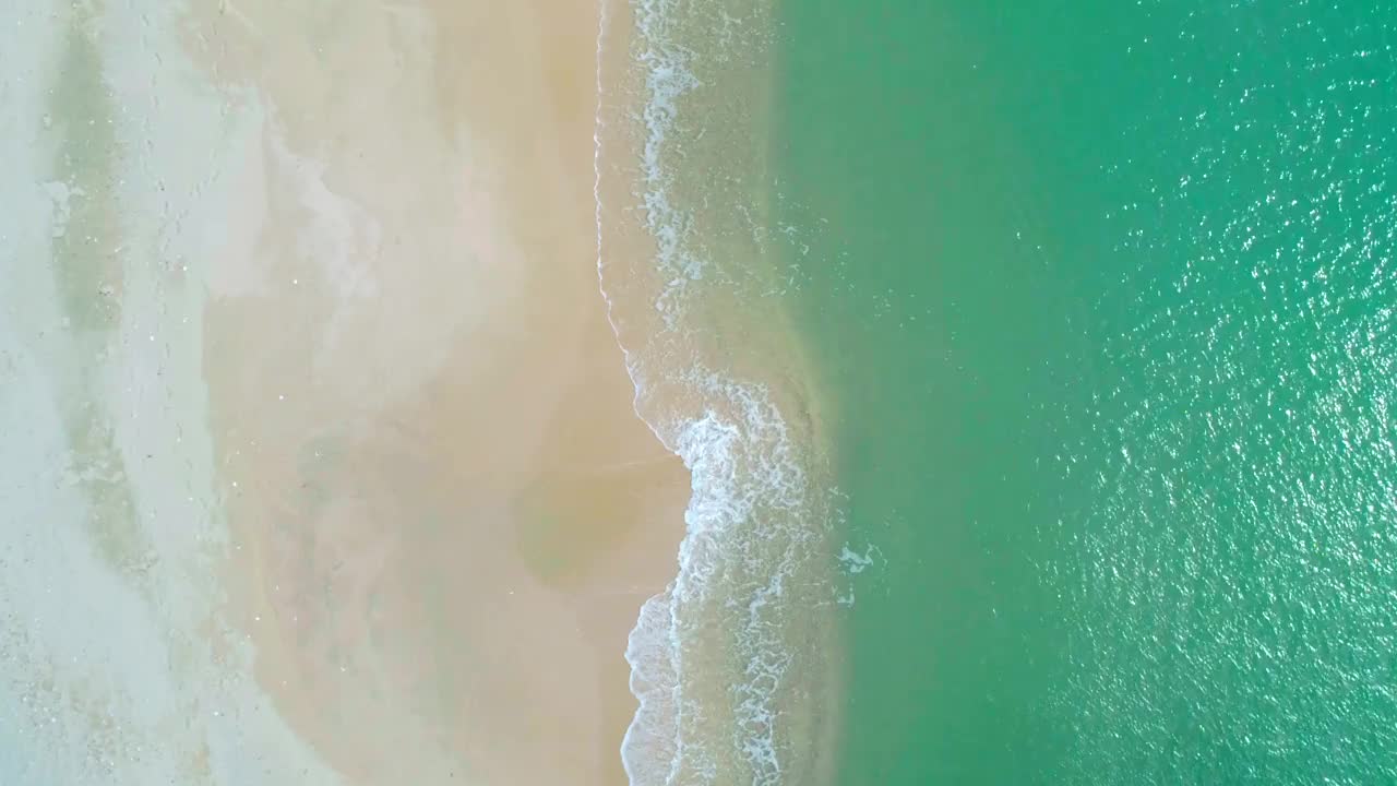 鸟瞰沙滩和蓝绿色海洋。在阳光明媚的日子里海浪到达海岸的俯视图。视频素材