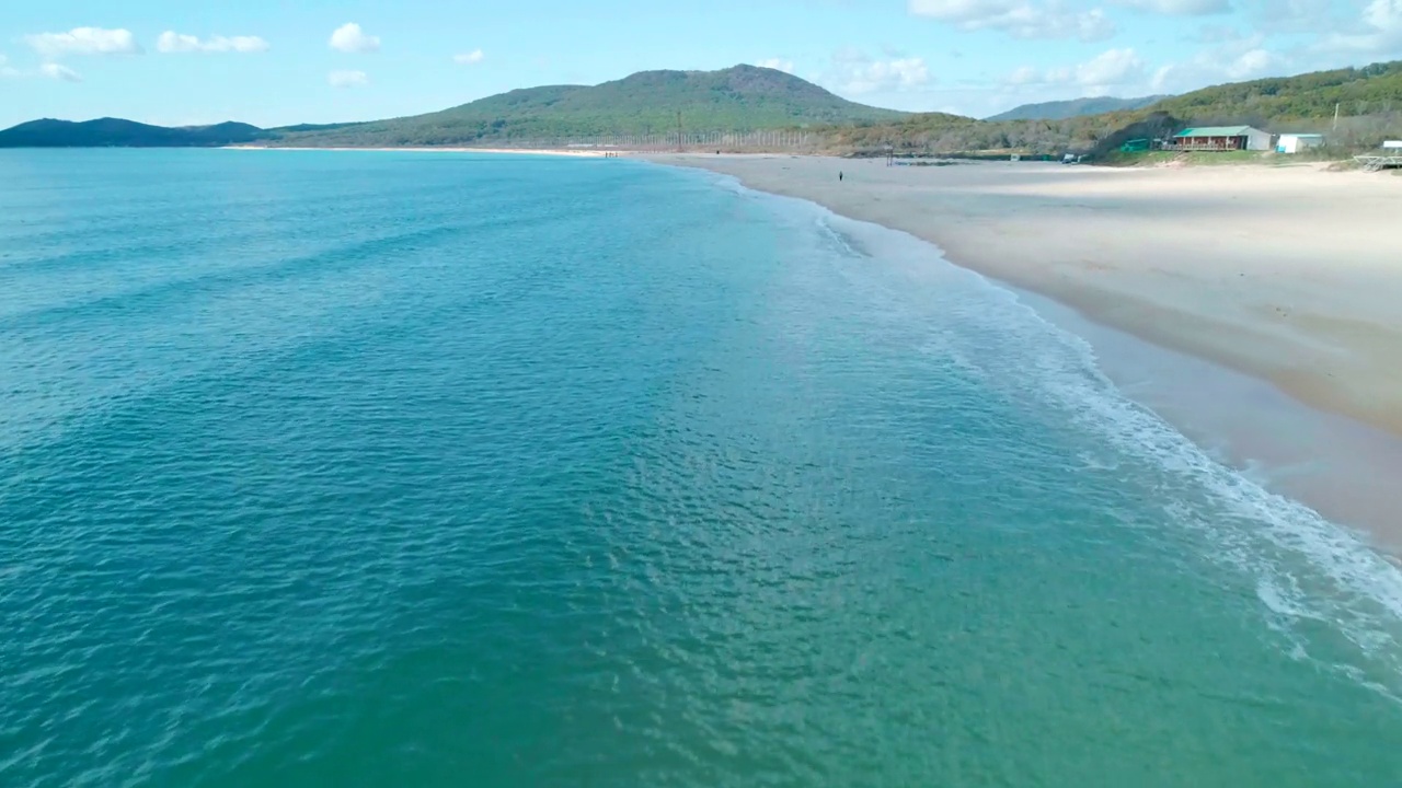 鸟瞰沙滩和蓝绿色海洋。海浪在晴天到达海岸。镜头向前移动视频素材