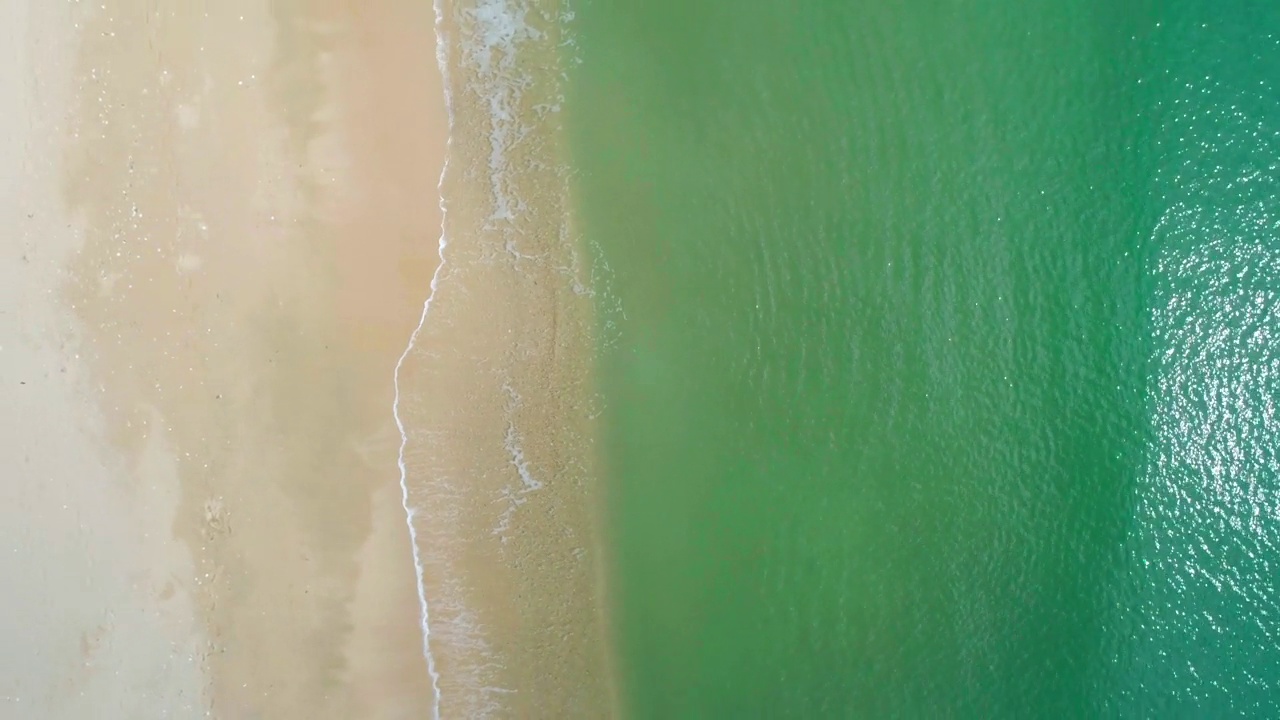 鸟瞰沙滩和蓝绿色海洋。在阳光明媚的日子里海浪到达海岸的俯视图。视频素材