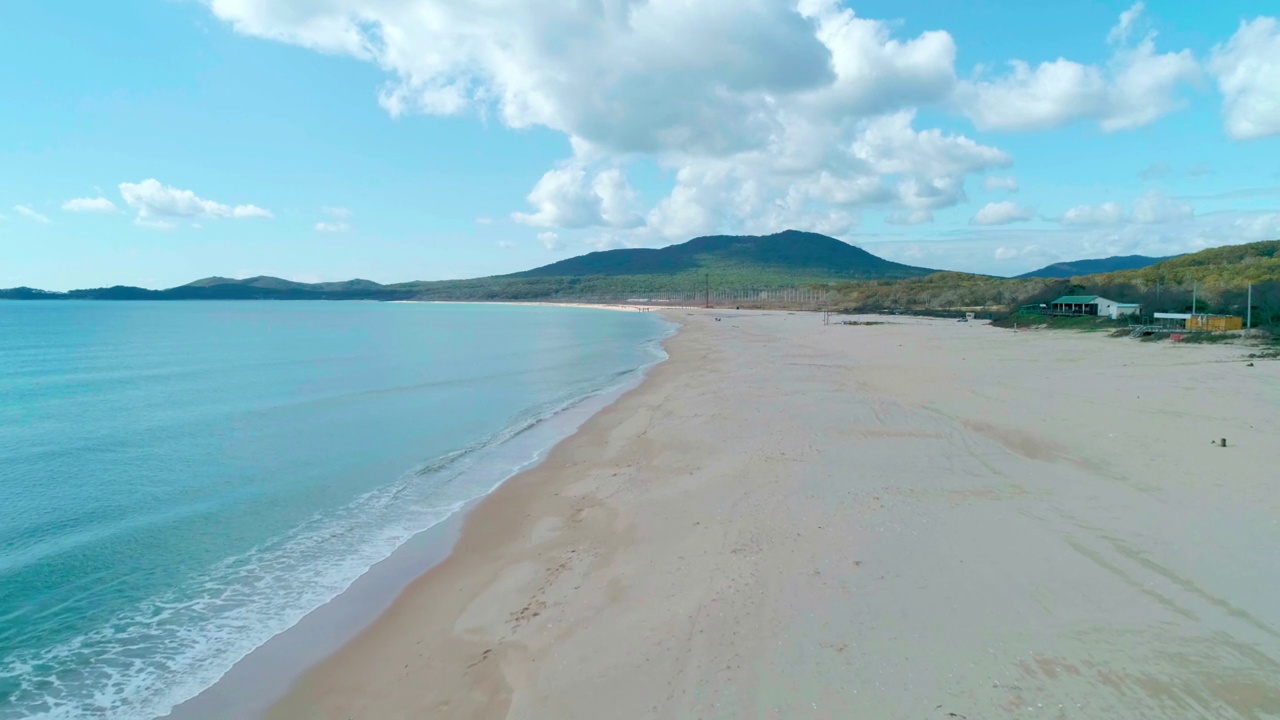 鸟瞰沙滩和蓝绿色海洋。在阴天到达海岸的海浪。镜头向前移动视频素材