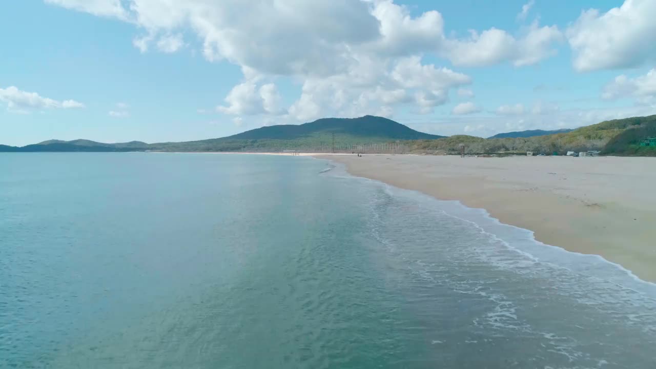 鸟瞰沙滩和蓝绿色海洋。在阴天到达海岸的海浪。镜头向前移动视频素材