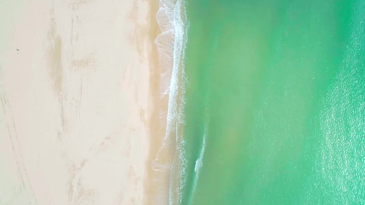 鸟瞰沙滩和蓝绿色海洋。在阳光明媚的日子里海浪到达海岸的俯视图。视频素材