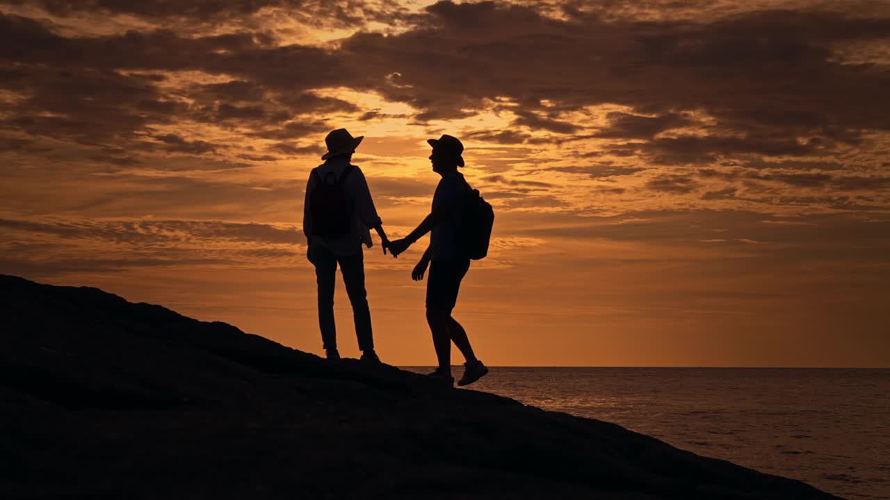 一对夫妇站在山顶上俯瞰夕阳下的大海视频素材