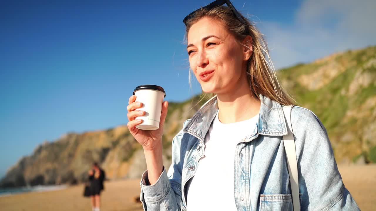 微笑的女人在海滩上用外卖杯喝咖啡视频素材