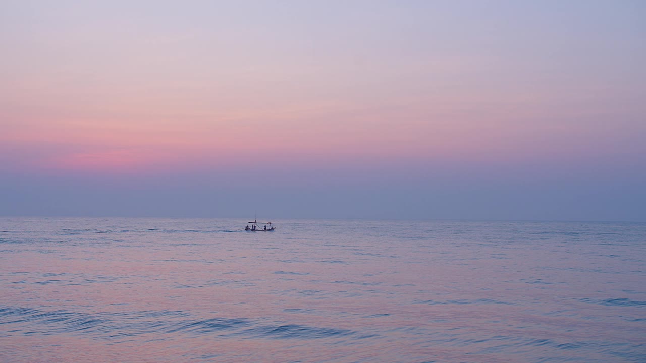 宁静的黄昏日落场景，在平静的海洋上，远处的渔船的小剪影映衬着彩色柔和的天空，宁静日落时海上的渔船剪影视频素材