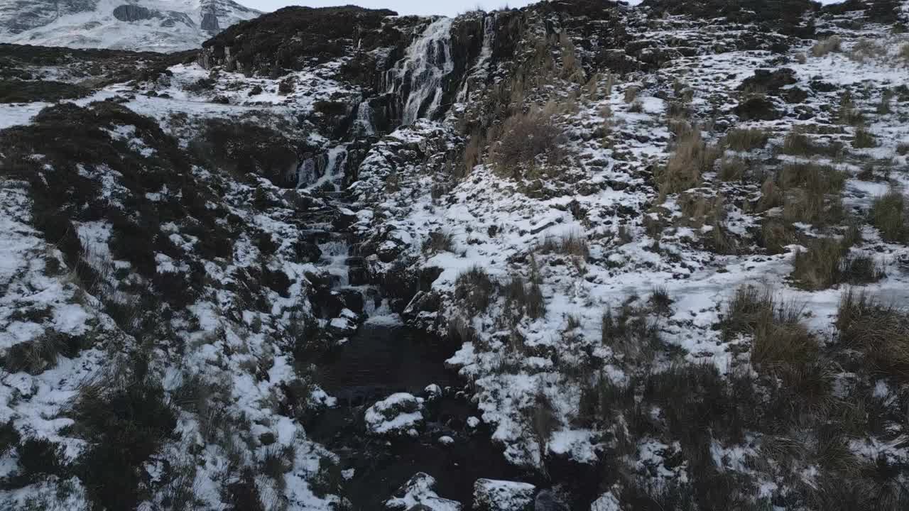 白雪覆盖的瀑布从岩石地形上倾泻而下，背景是山脉，拍摄于苏格兰的天空新娘面纱瀑布视频素材