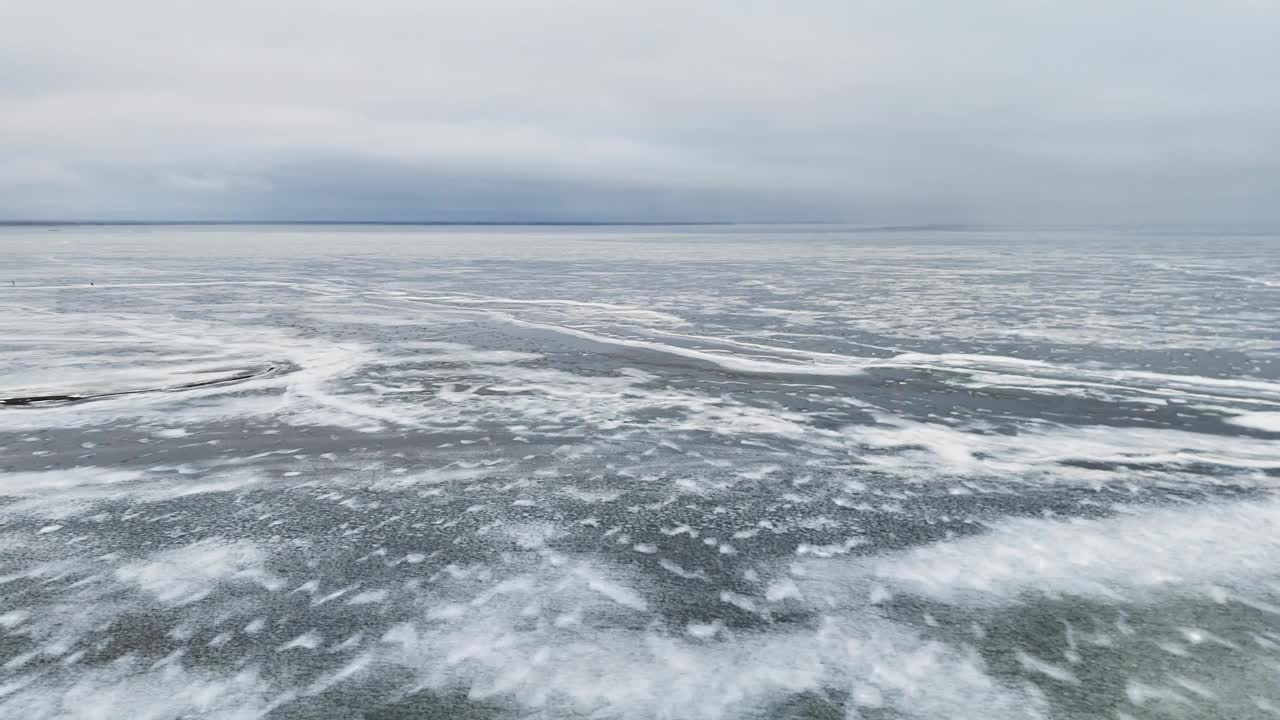 在多云的天空下，广阔的冰冻湖泊，在立陶宛可以看到轻微的积雪和冰的图案，鸟瞰图视频素材