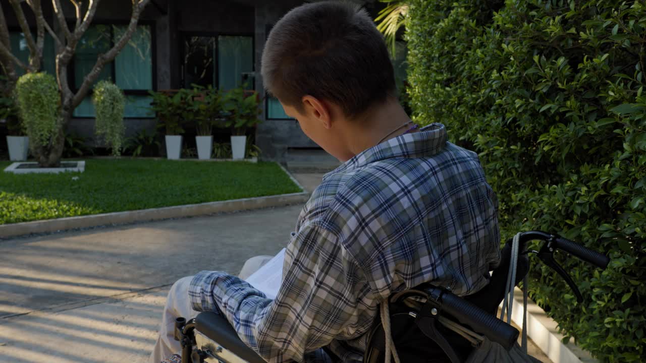 成年女性经历了残疾并使用轮椅，在公园小路提供的宁静通道中找到了安慰。她全神贯注地阅读，体现了赋权视频下载