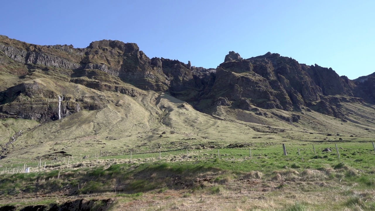 郁郁葱葱的冰岛风景，崎岖的悬崖和清澈蓝天下的小瀑布视频素材