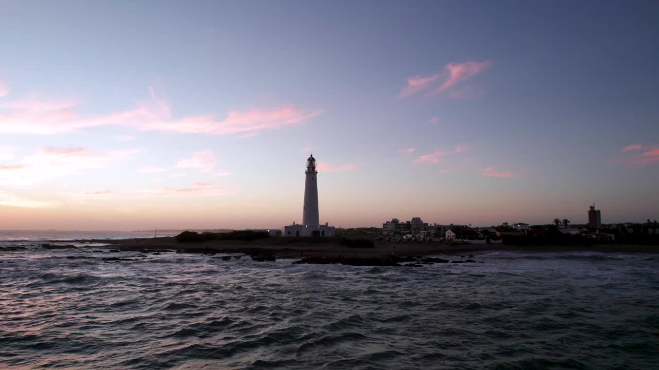 葡萄牙法罗尔岛的灯塔映衬着夕阳的天空，海浪拍打着海岸线视频素材