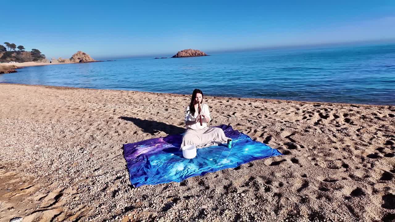 迷人的年轻女子在平静空旷的沙滩上吹着木笛视频素材