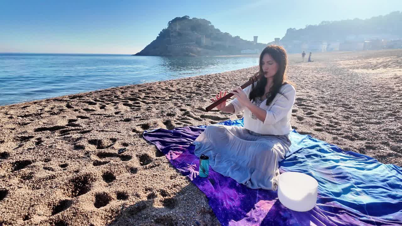 迷人的年轻女子在平静空旷的沙滩上吹着木笛视频素材