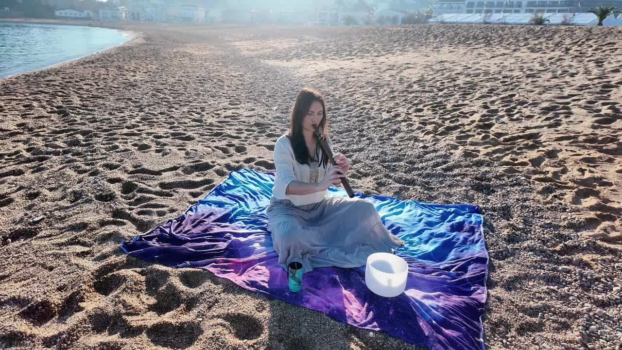 迷人的年轻女子在平静空旷的沙滩上吹着木笛视频素材