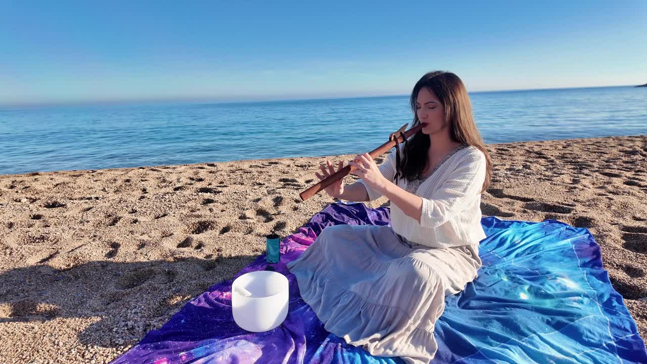 迷人的年轻女子在平静空旷的沙滩上吹着木笛视频素材