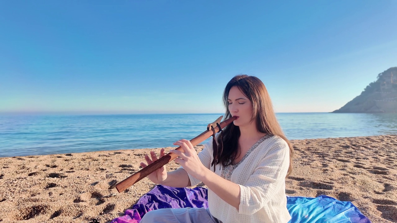 迷人的年轻女子在平静空旷的沙滩上吹着木笛视频素材