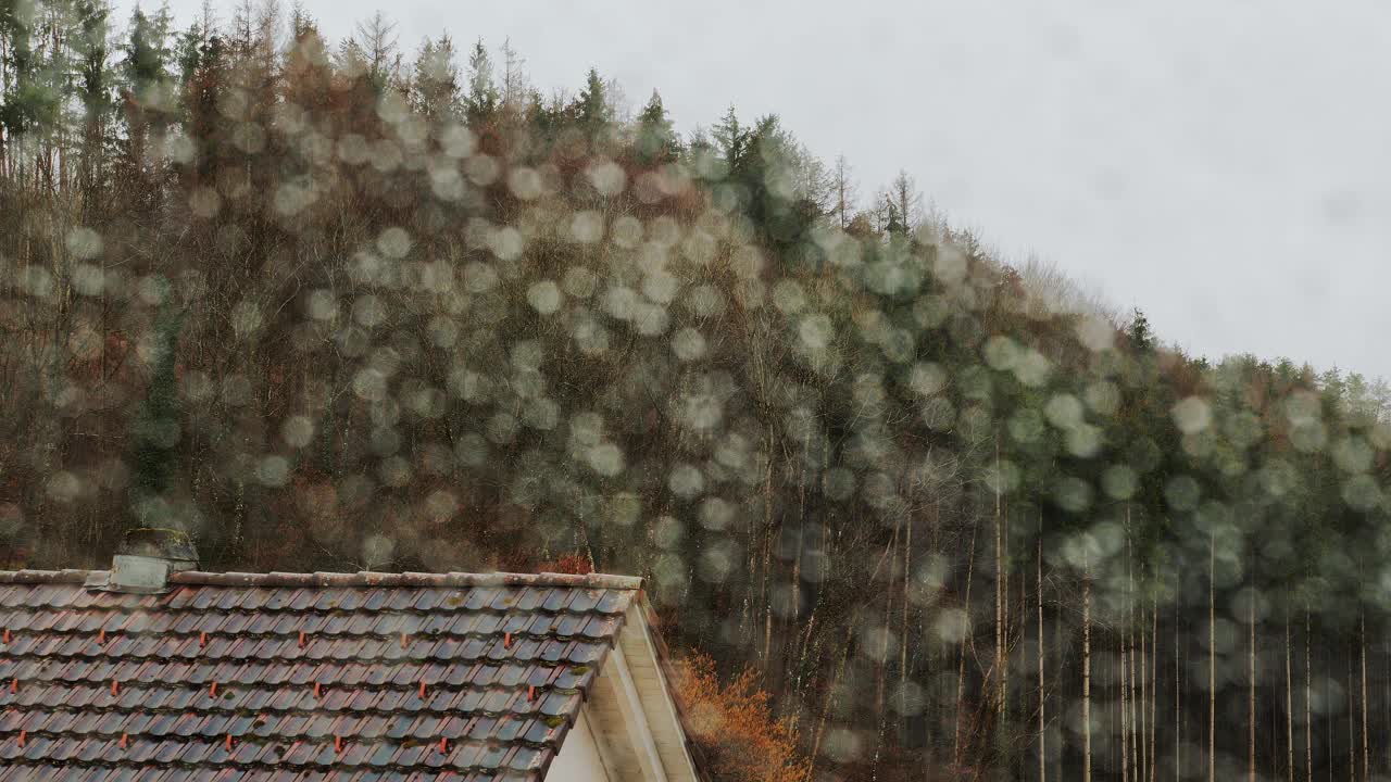 雨落在以森林和房子为背景的玻璃窗上。多雨的天气视频素材