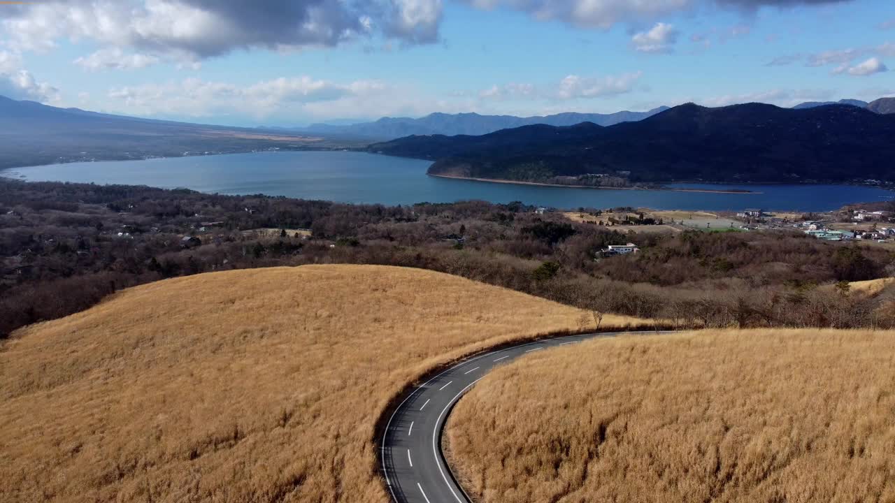 一条蜿蜒的道路穿过金色的草地，远处是湖泊和山脉，鸟瞰图视频素材